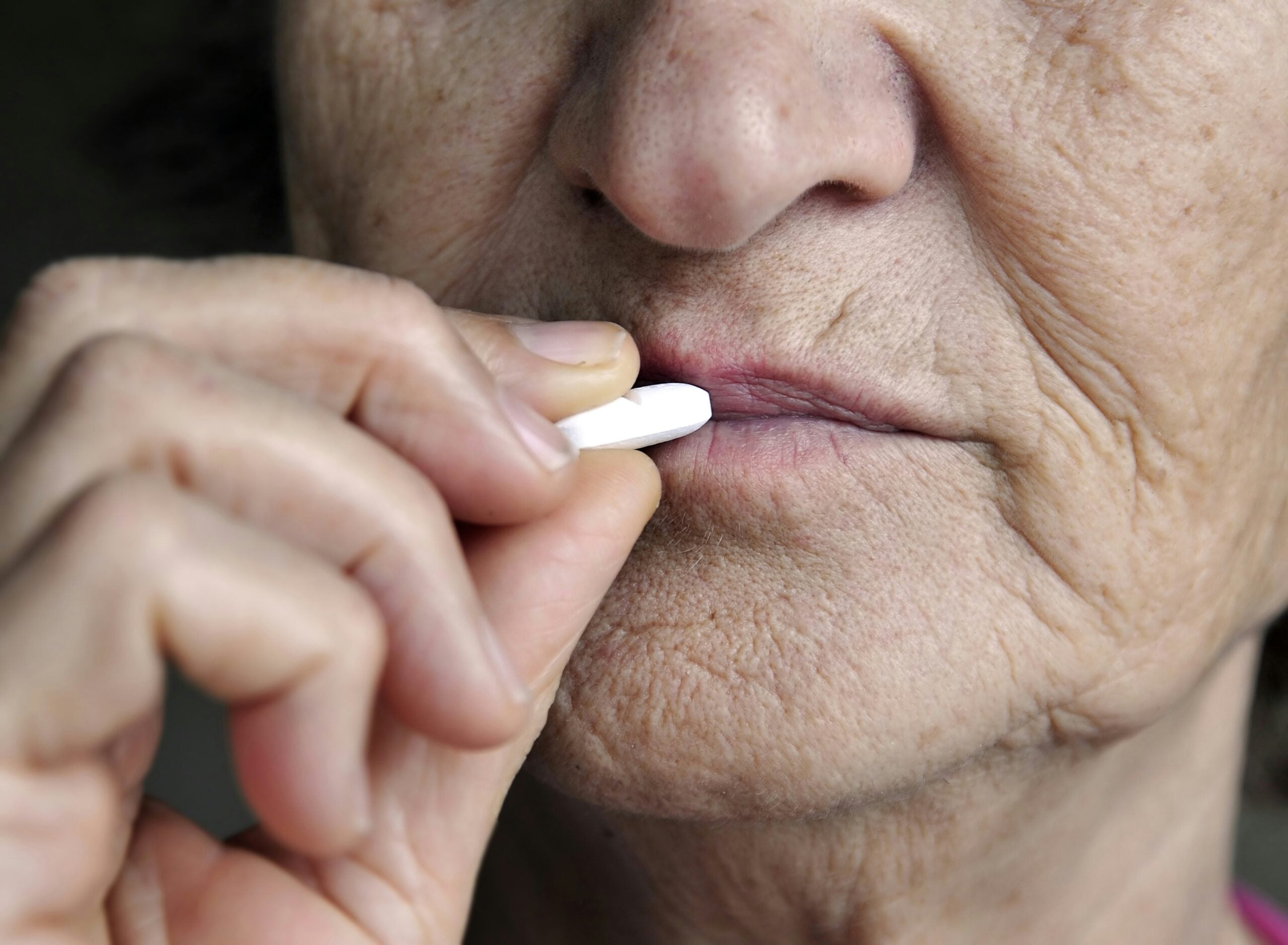 Close-up of an older person holding a white pill near their lips, appearing about to take medication. The image highlights the person’s wrinkled skin and focused expression, subtly evoking the health considerations that often accompany planning for retirement savings.