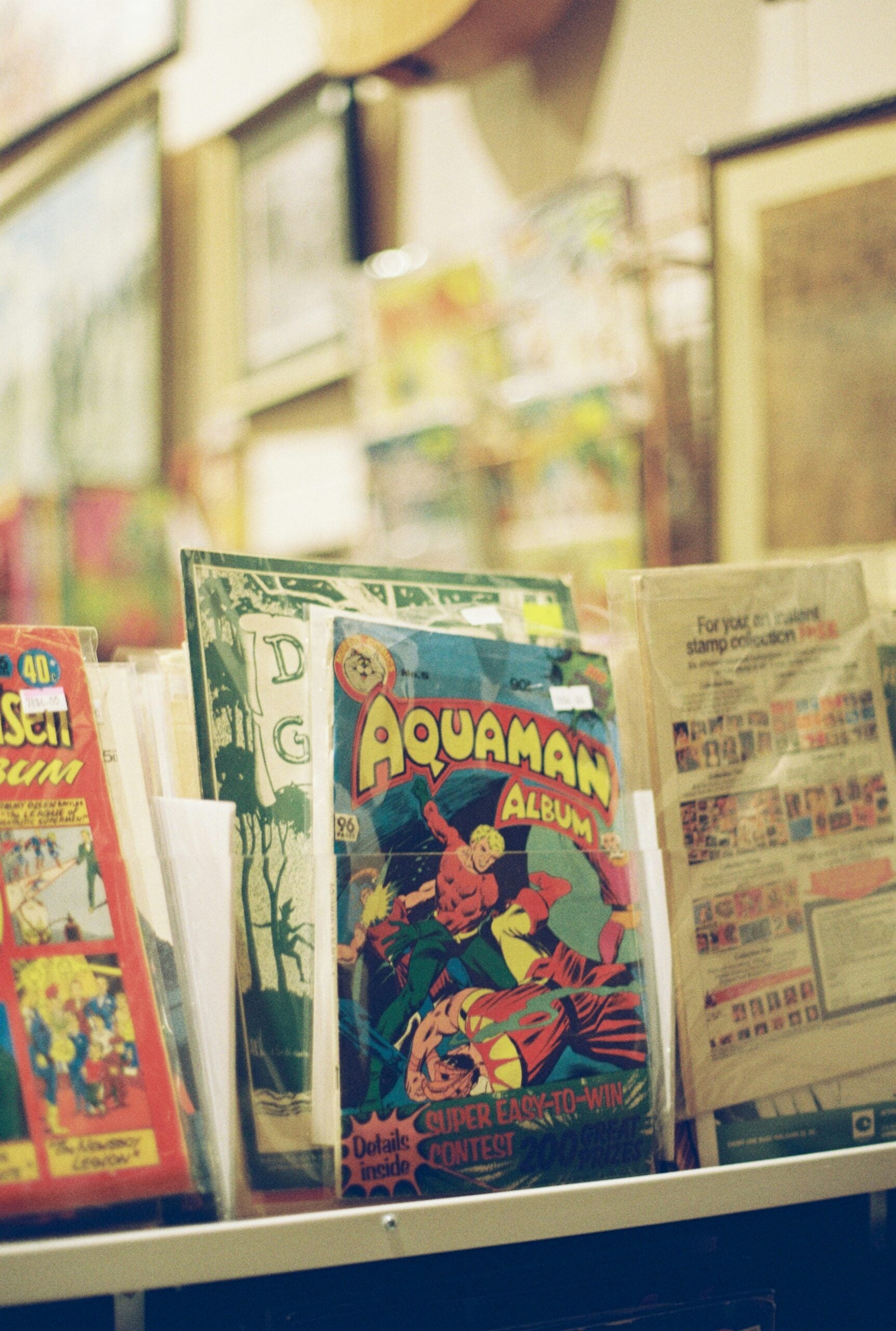A close-up of vintage comic books, with an Aquaman comic prominently displayed in front, surrounded by other colorful comics in protective sleeves on a display rack.
