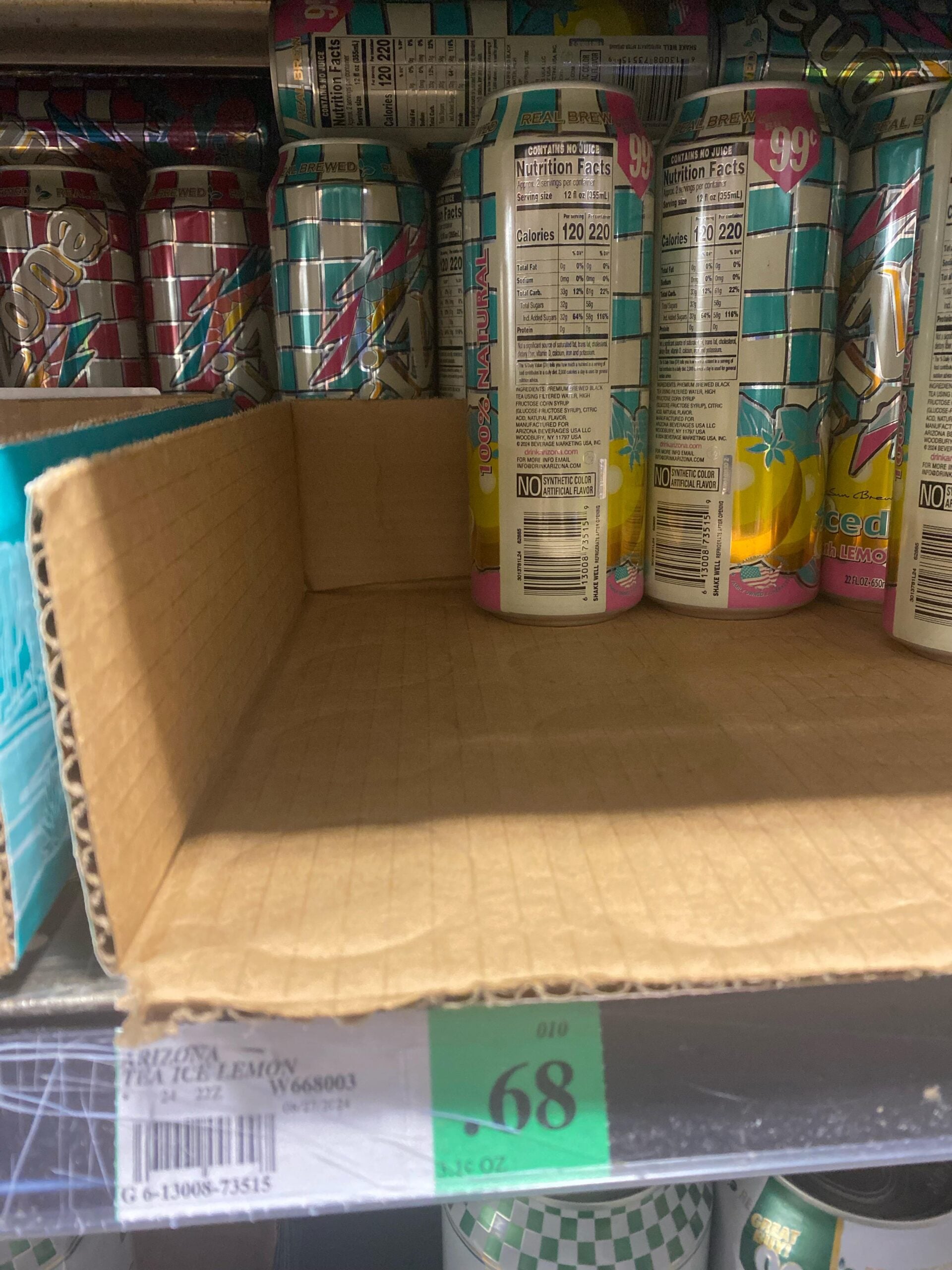 A mostly empty cardboard tray sits on a store shelf, holding a few tall cans of Arizona Mucho Mango juice drink. The shelf tag below shows a price of 68 cents.