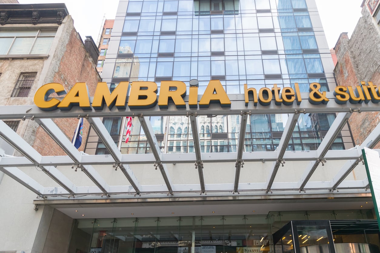 Cambria Hotel & Suites entrance with large yellow sign, glass canopy, and modern glass building facade in an urban setting—showcasing the distinctive style found among top hotel chains.
