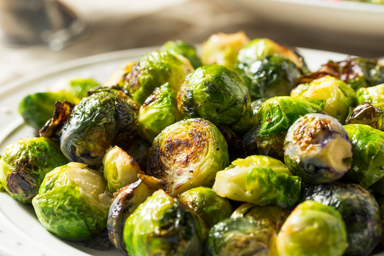 A close-up of roasted Brussels sprouts on a white plate, showing their crispy, golden-brown edges and green color—a classic example of the kinds of Foods People Learn to Appreciate Later in Life.