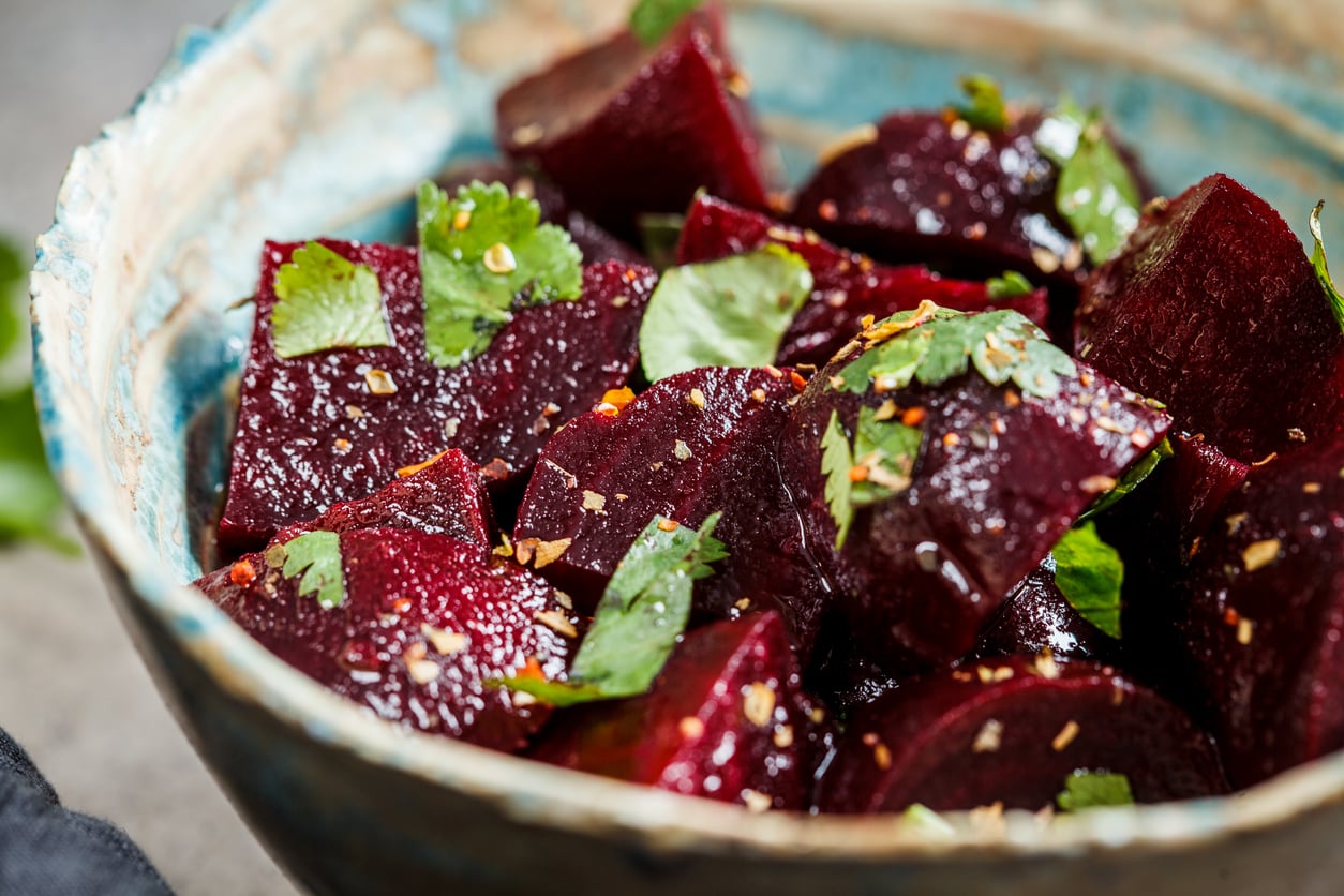 A ceramic bowl filled with chunks of cooked beets, garnished with fresh cilantro and seasoning—a classic example of foods people learn to appreciate later in life.