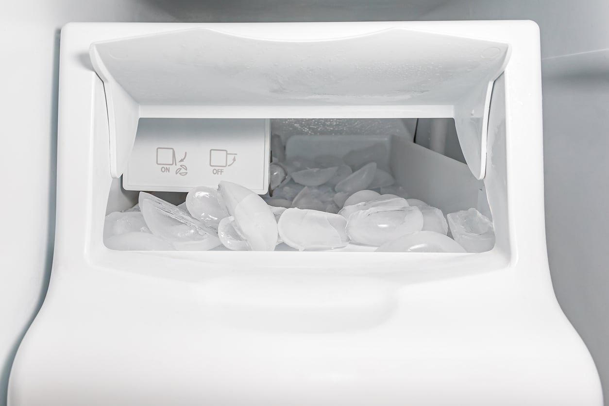 A white automatic ice maker filled with ice cubes, showing ON and OFF buttons inside the compartment.