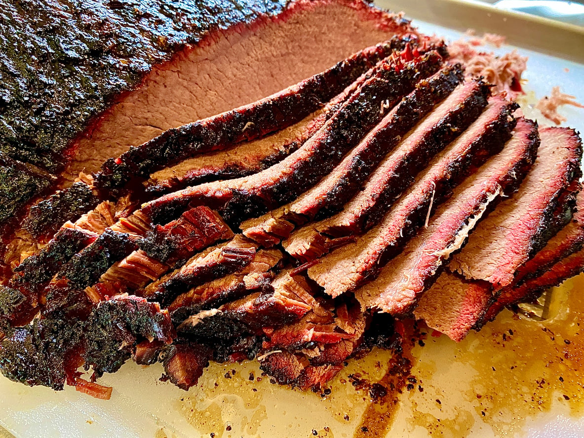 Sliced smoked brisket on a cutting board with a dark outer bark and juicy, pink interior—a mouthwatering highlight among classic comfort foods.