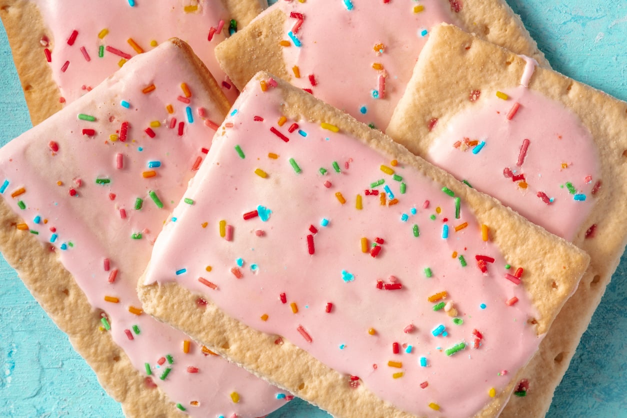 Pink-frosted rectangular pastries with colorful sprinkles stacked on a blue background.