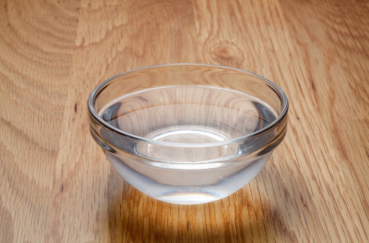 A clear glass bowl filled with water sits on a wooden surface, casting a soft shadow.