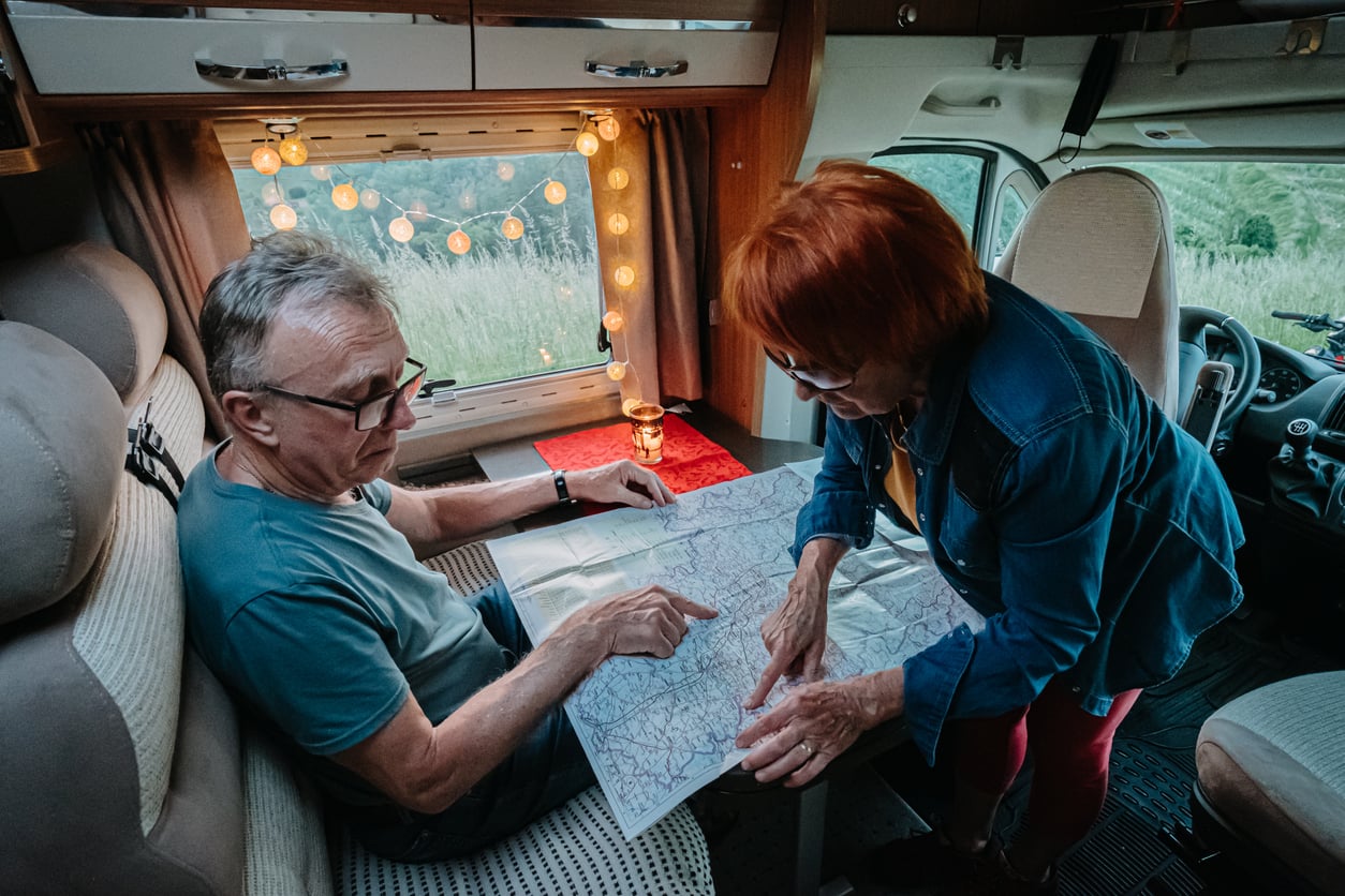 An older man and woman inside a camper van look at a map together. Going through one of the Baby boomer hassles.