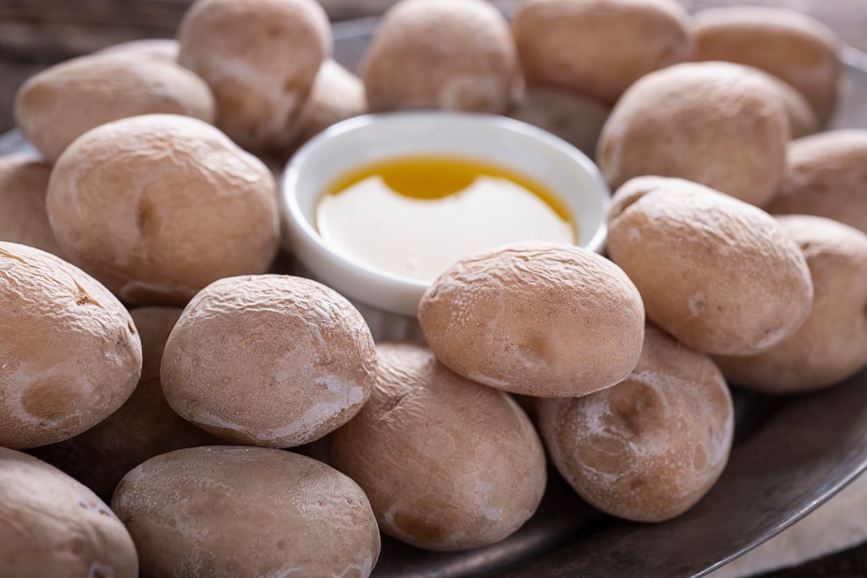 A plate of small, salted potatoes surrounds a white dish of yellow olive oil, ready for dipping.