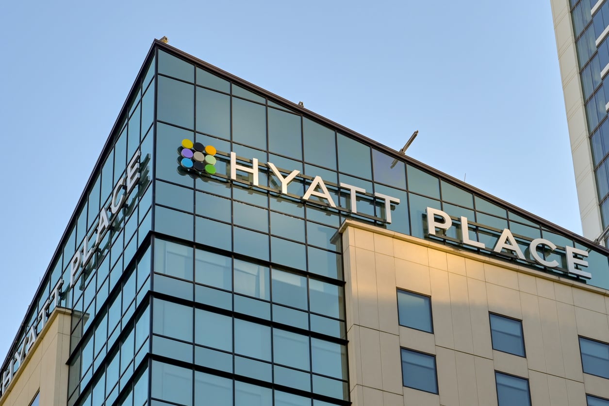 The image shows the top corner of a modern building with large glass windows and the sign “Hyatt Place” displayed prominently on the facade, representing one of the well-known hotel chains.