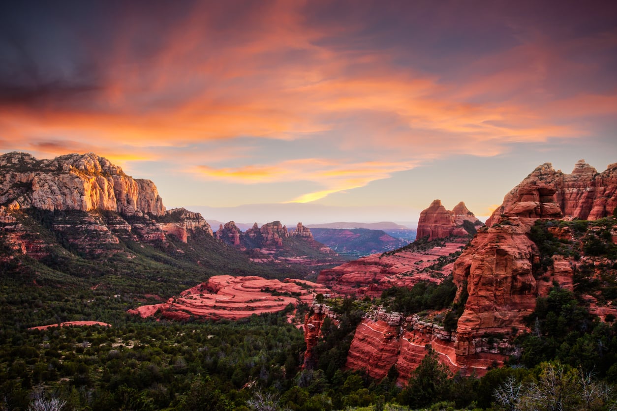 Sunset over red rock formations and green valleys in Sedona, Arizona, with dramatic clouds and colorful sky.
