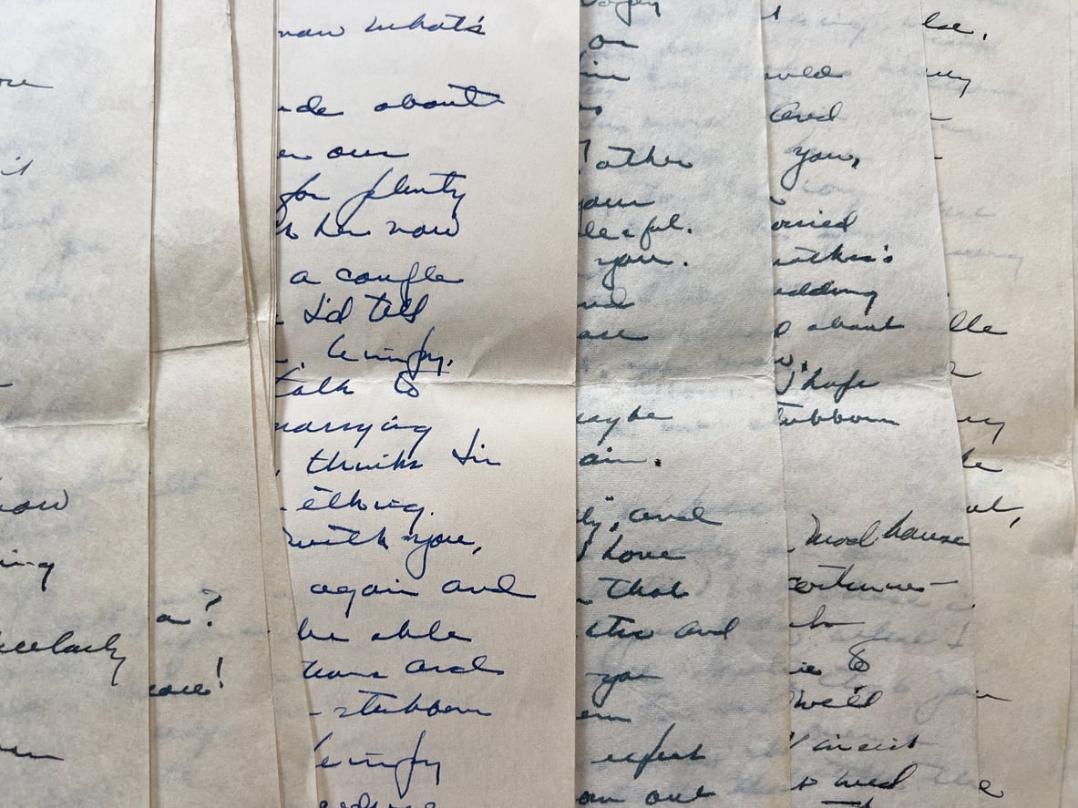 Close-up of vintage handwritten letters in blue ink on aged, partially transparent paper, overlapped in vertical strips. The writing is cursive and mostly illegible due to layering.