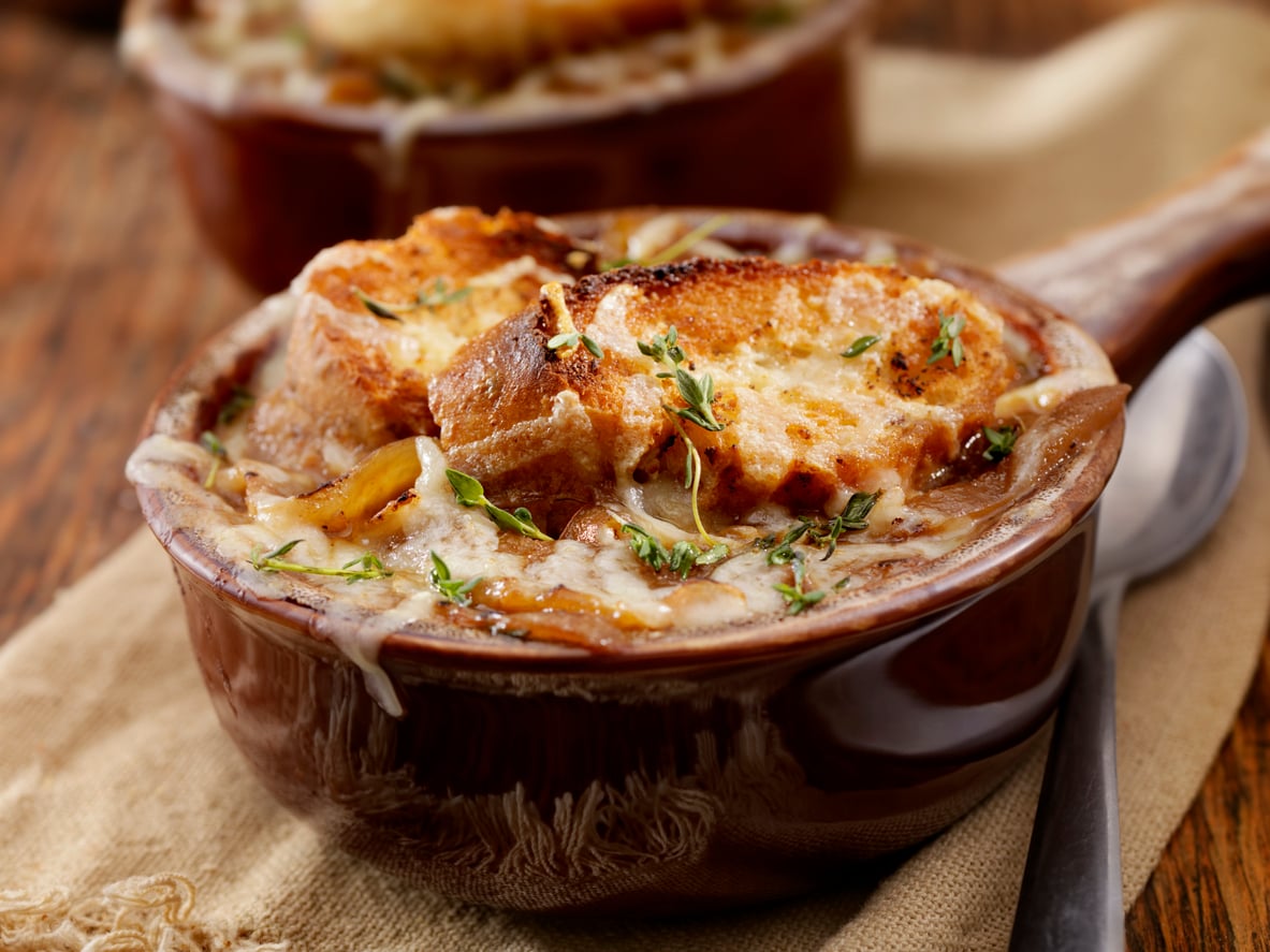 A bowl of French onion soup topped with toasted bread, melted cheese, and fresh thyme, served on a rustic napkin with a spoon nearby.