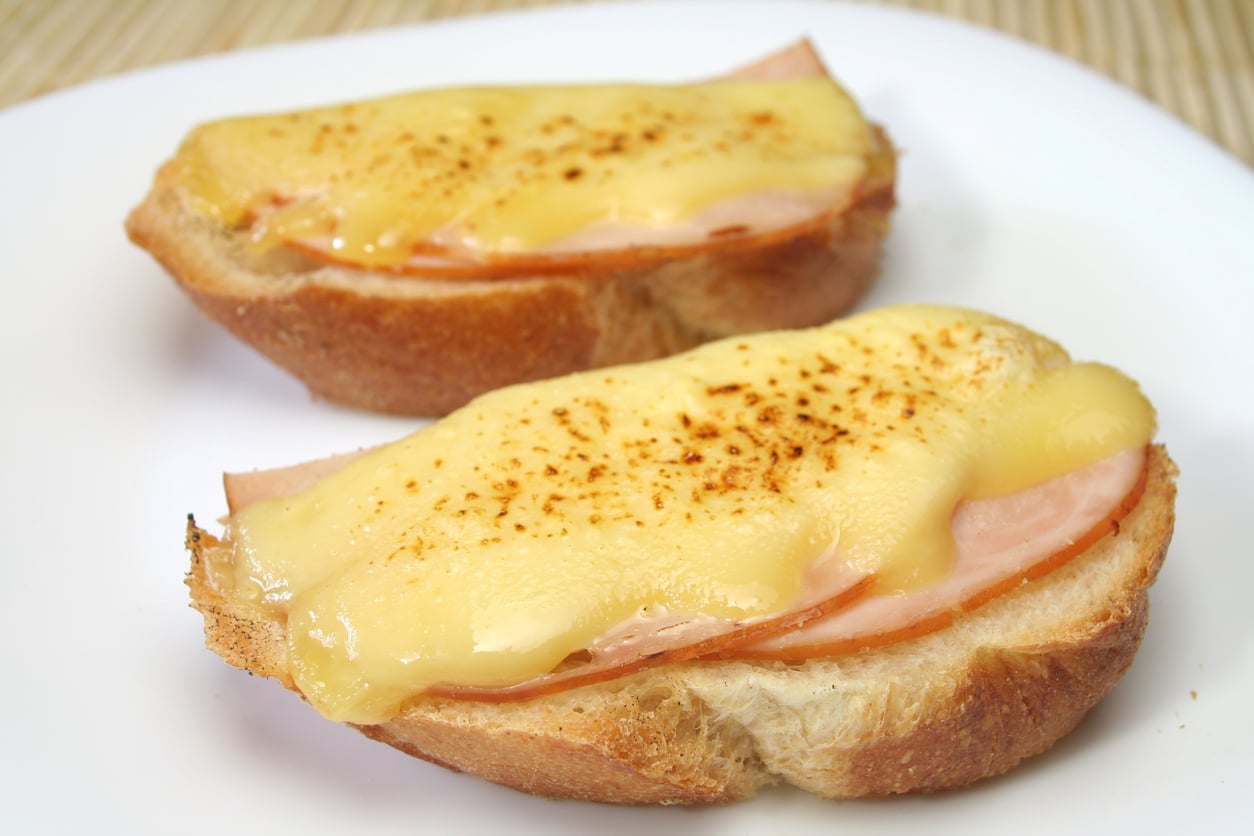 Two slices of bread topped with ham and melted cheese, served on a white plate.