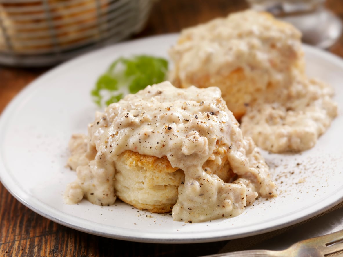 Two biscuits topped with creamy sausage gravy and black pepper sit on a white plate with a garnish of parsley in the background.