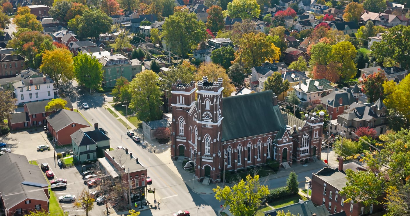 Aerial view of a town with a large red brick church, tree-lined streets, houses, and colorful autumn foliage.