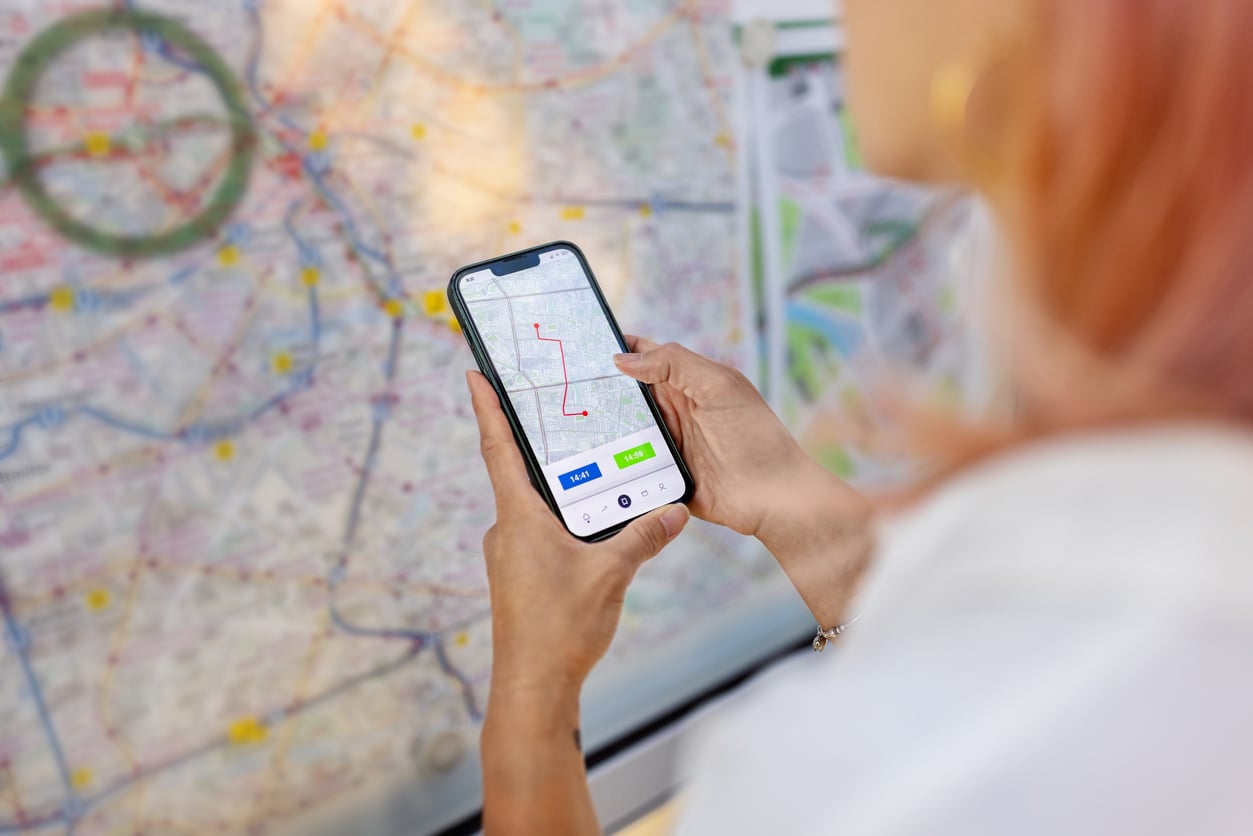 A person holds a smartphone showing a navigation route, standing in front of a large map on a wall—carefully planning their journey to avoid common vacation mistakes.
