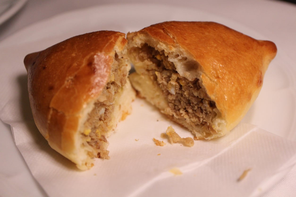A baked pastry cut in half, revealing a savory filling of ground meat and egg, sits on a white napkin atop a plate—one of the restaurant specialties that delights guests with its comforting flavors.