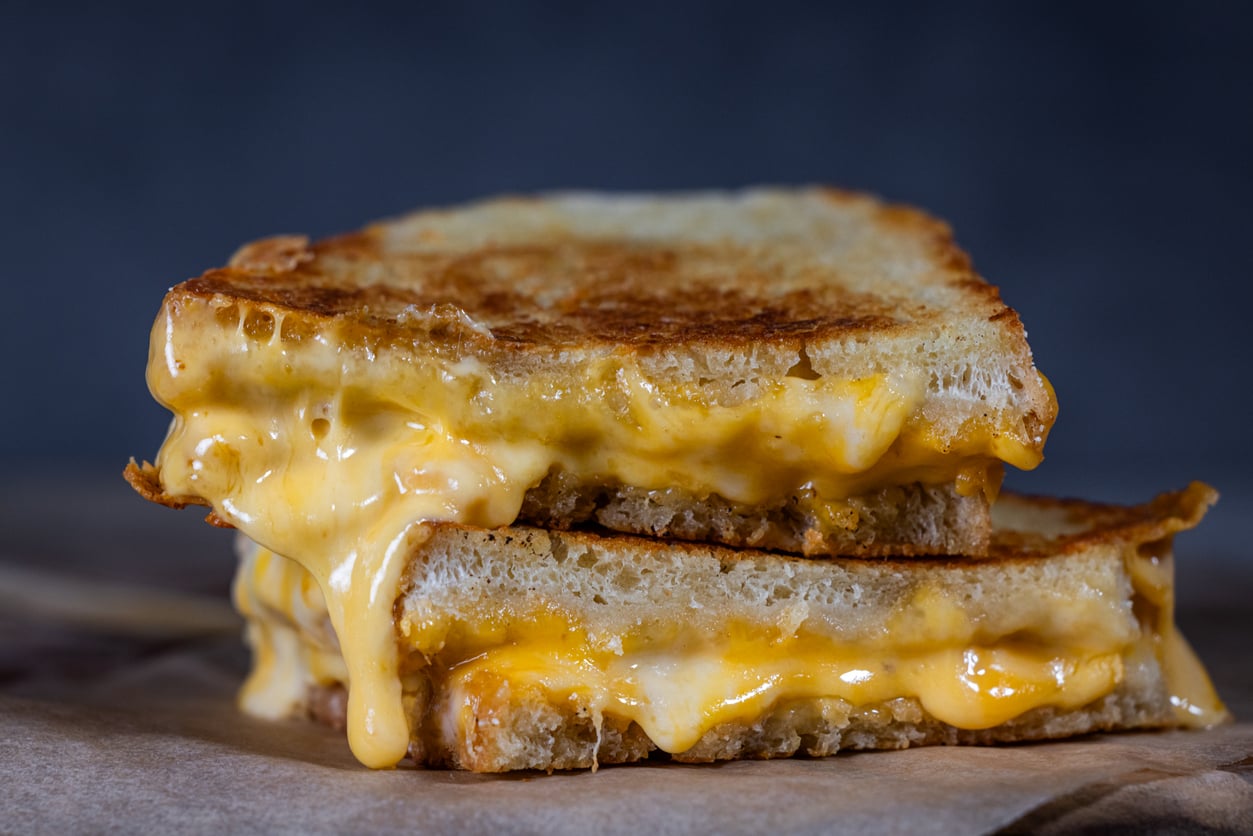 A close-up of a grilled cheese sandwich cut in half, with golden, crispy bread and melted cheese oozing out between the slices.