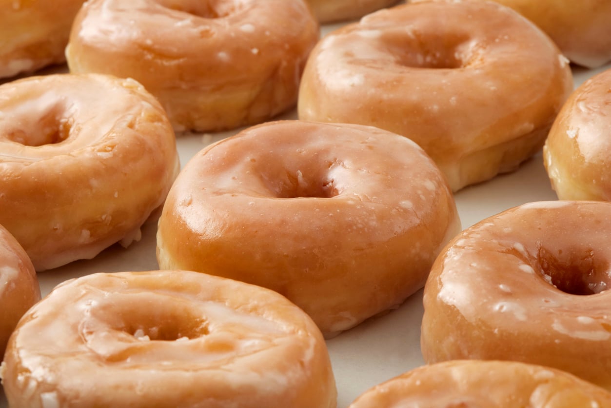 A close-up of several glazed donuts arranged in rows, showing their shiny, sugary coating and classic ring shape.