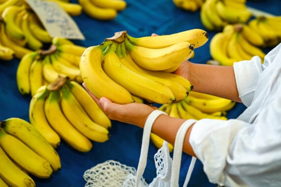 A person holds a bunch of ripe yellow bananas at a market&mdash;one of those everyday foods that used to be considered fancy&mdash;with more bananas displayed on a blue table in the background.