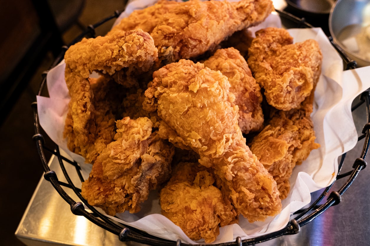 A basket filled with pieces of golden, crispy fried chicken arranged on white parchment paper.