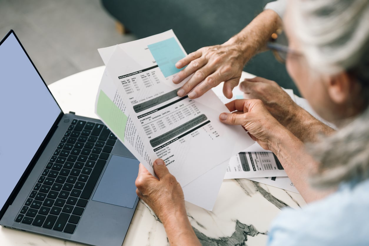 Two people review printed financial documents at a marble table next to an open laptop, discussing data and retirement money habits as one person points to a section on the papers.