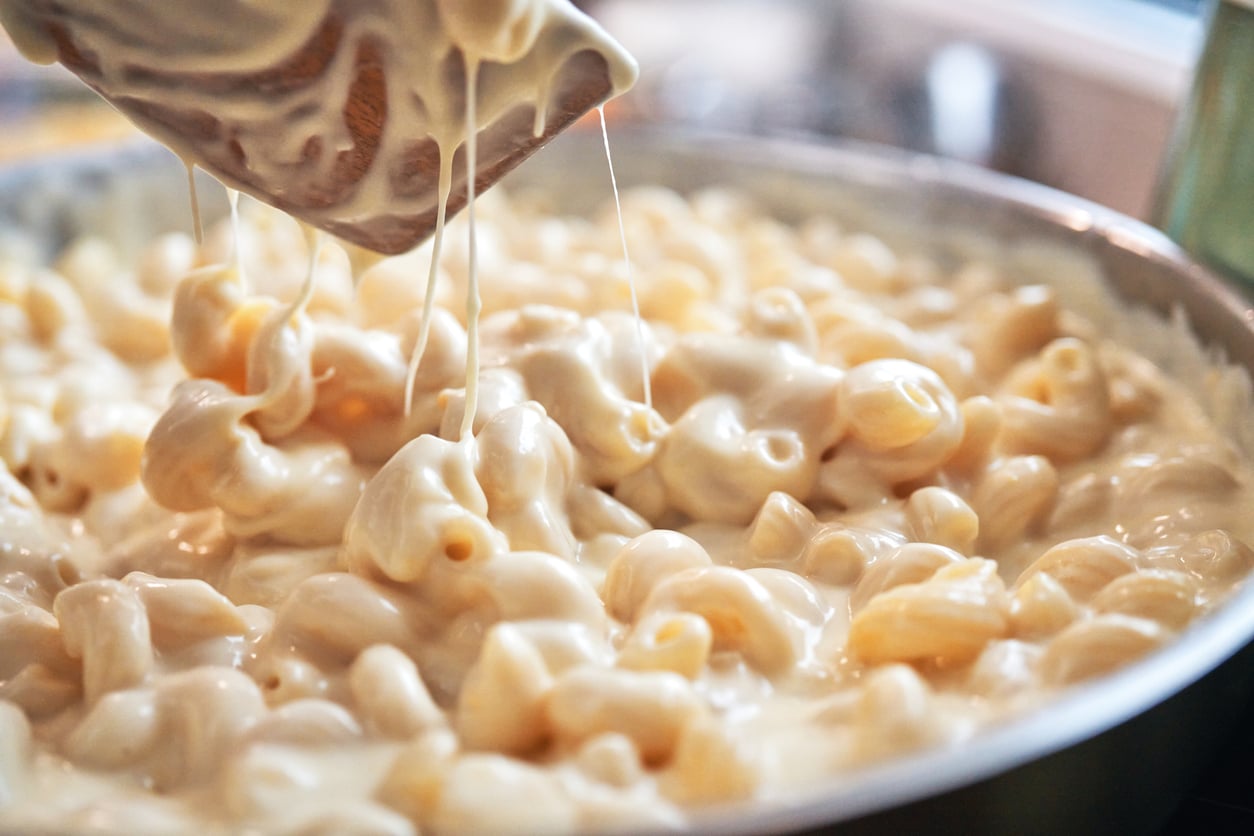 Close-up of creamy macaroni and cheese being stirred, with melted cheese stretching between noodles in a pan.