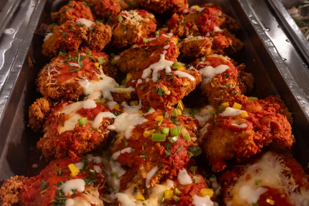 A tray filled with breaded chicken cutlets topped with marinara sauce, melted cheese, and garnished with chopped green onions and herbs—one of the classic foods to order for any gathering or family meal.