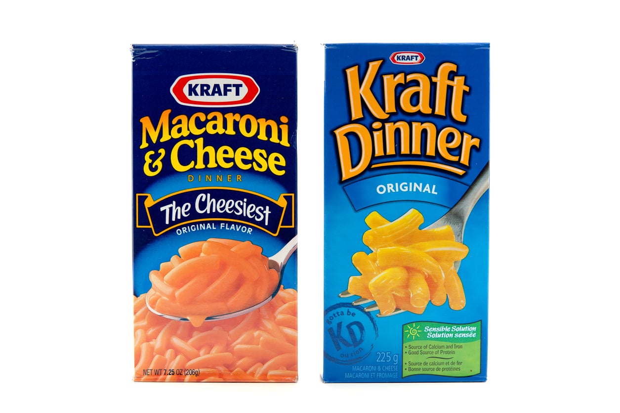Two boxes of Kraft macaroni and cheese; one labeled “Kraft Macaroni & Cheese Dinner” and the other “Kraft Dinner Original.” Both show cooked macaroni and cheese on a fork.