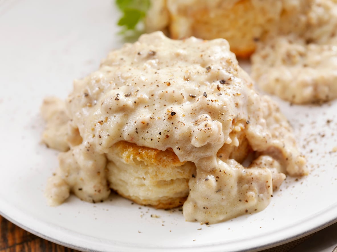 A flaky biscuit topped with creamy sausage gravy, sprinkled with black pepper, served on a white plate.