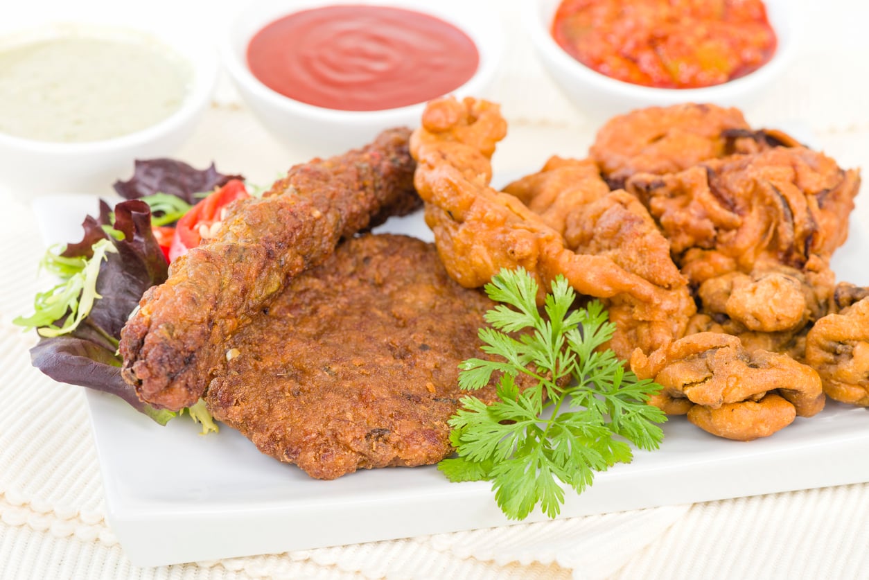 A white plate with assorted fried foods, leafy greens, and a sprig of cilantro, with three bowls of dipping sauces in the background.