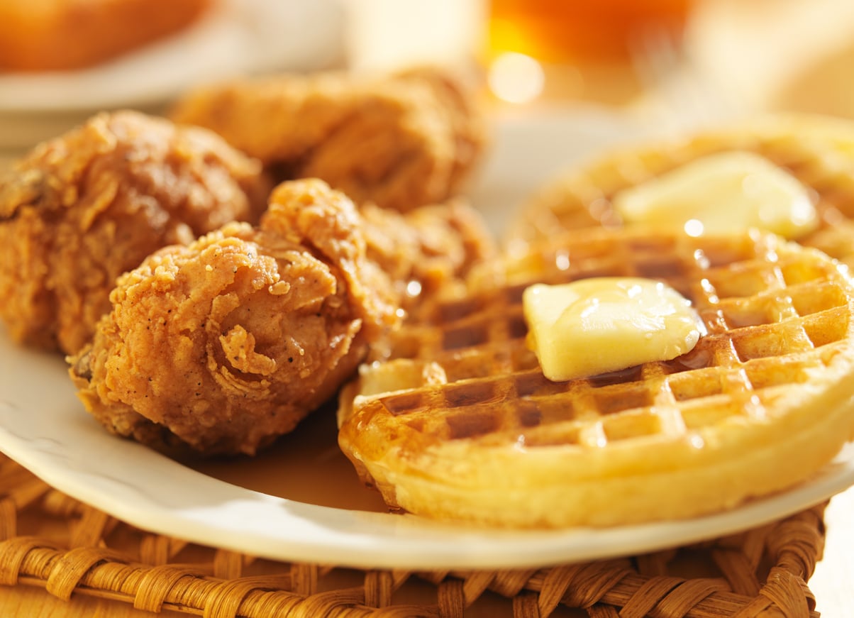 A plate with crispy fried chicken pieces and two waffles topped with melting butter and syrup.