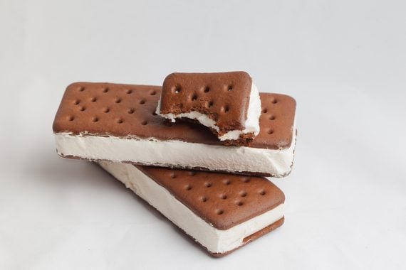 Two chocolate ice cream sandwiches are stacked. The top sandwich has a bite taken out, revealing vanilla ice cream between the chocolate layers. The background is plain white.