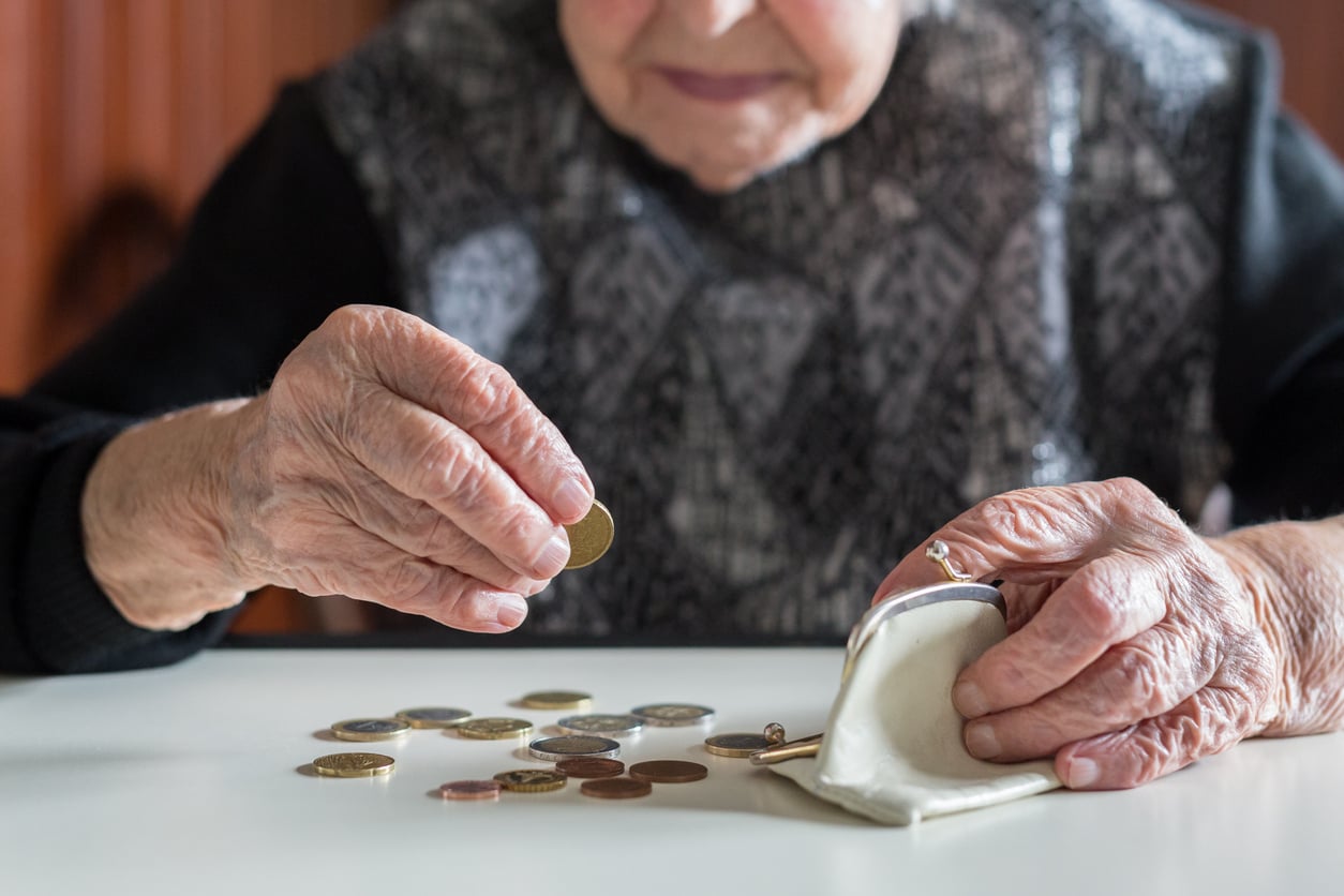 An elderly person sits at a table, holding a coin and counting loose change from a small white coin purse. The scene suggests careful money management or budgeting, reflecting thoughtful retirement money habits.