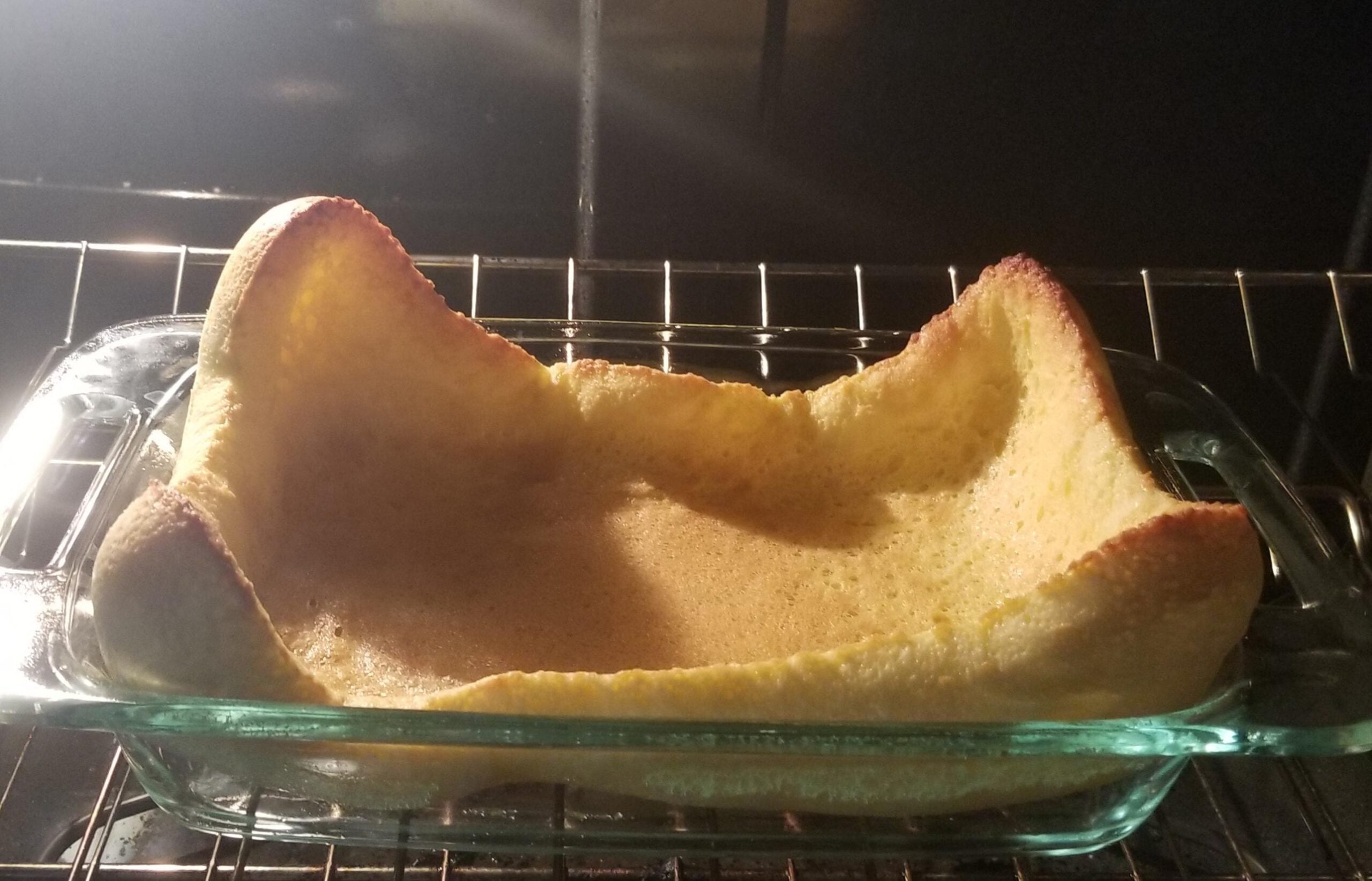 A Dutch baby pancake baking in a glass dish in the oven, with puffed, golden-brown edges and a flat center.