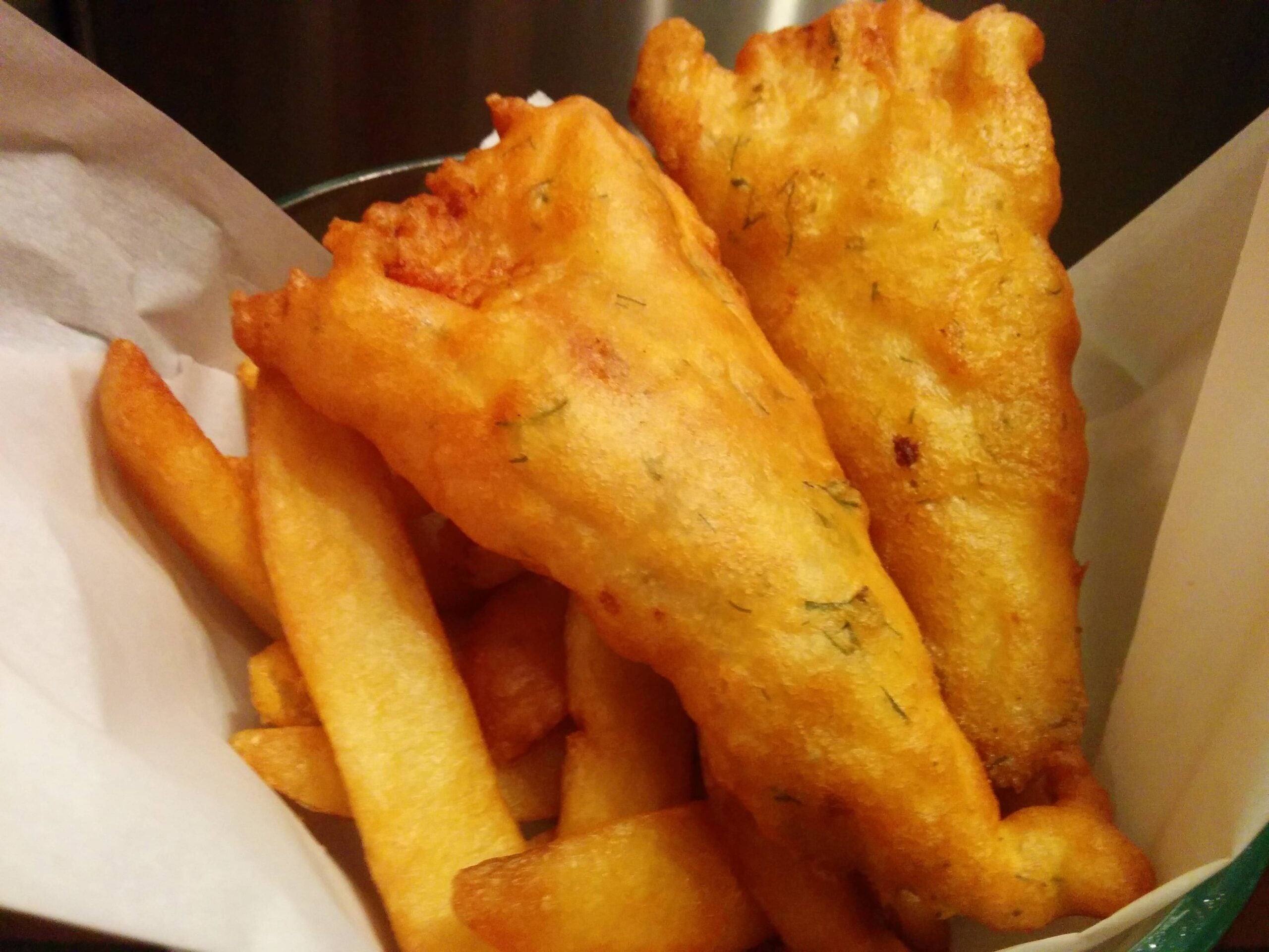 Golden battered fish fillets and thick-cut fries in a white paper-lined basket.