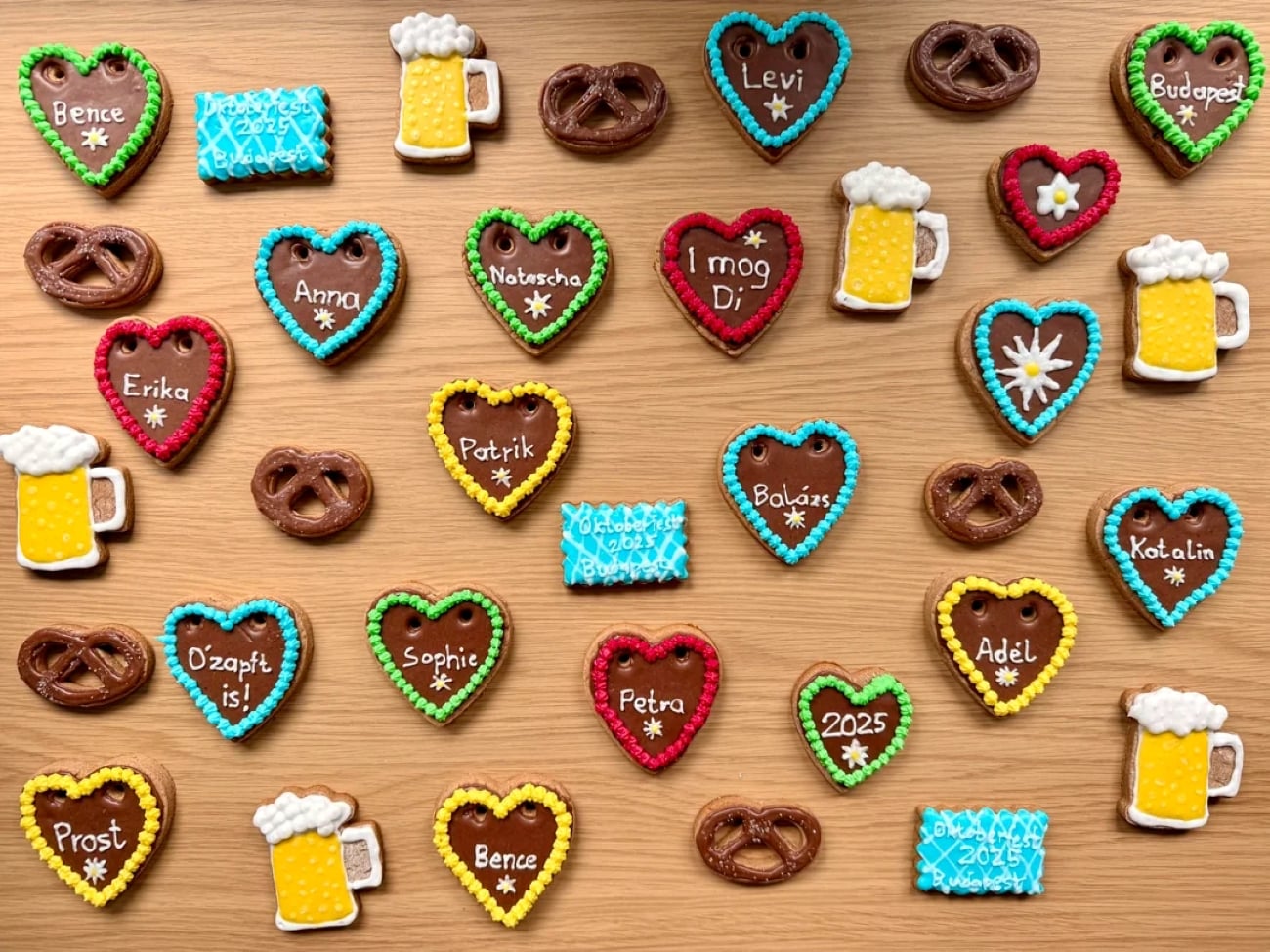 Assorted gingerbread cookies shaped like hearts, pretzels, beer mugs, and plaques with colorful icing, names, and words, arranged on a wooden surface.