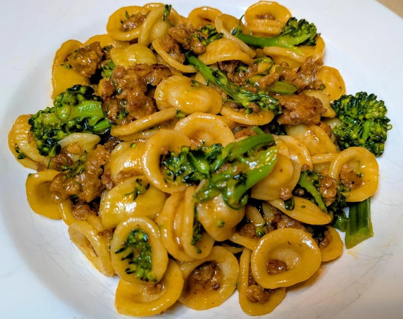 Orecchiette pasta with sausage and broccoli rabe, tossed in a savory sauce, served on a white plate—just like the mouthwatering dishes you see in Photos Of Pasta.