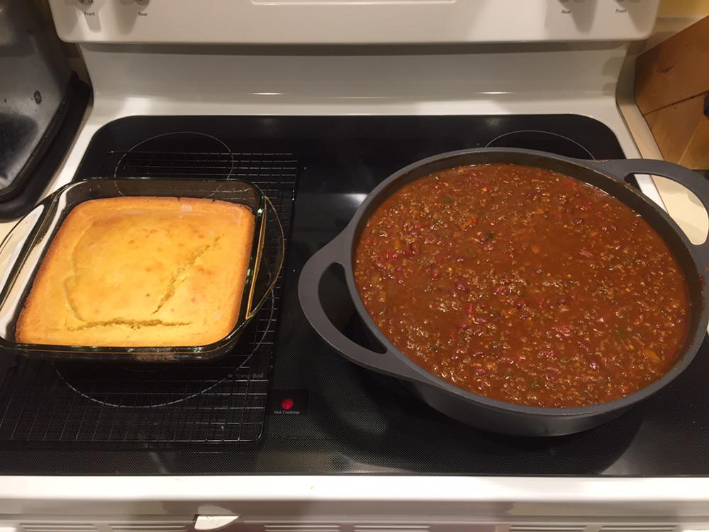 A pan of golden cornbread and a large pot of chili with beans and ground meat sit side by side on a stovetop.