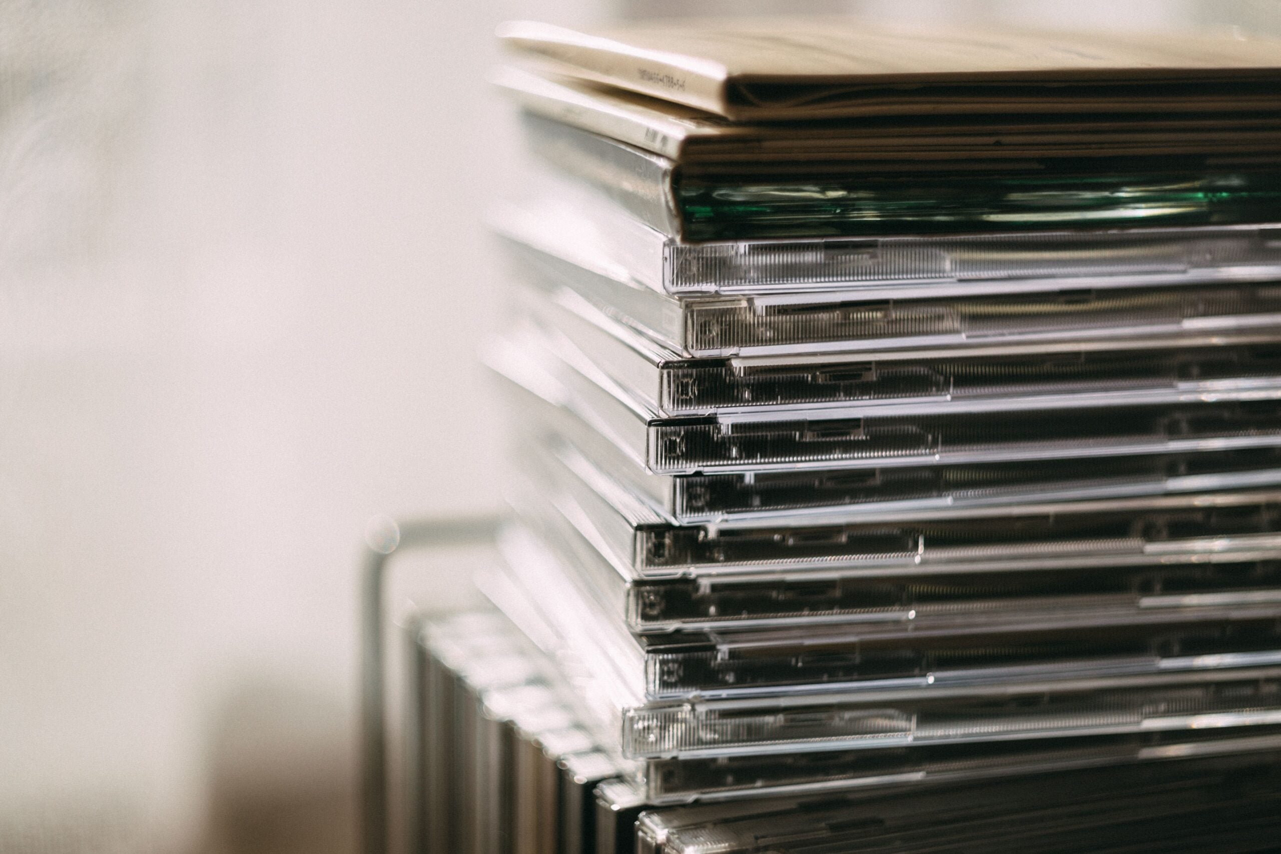 A close-up of a tall stack of compact disc (CD) cases, some with visible discs inside, with a soft, blurred background.