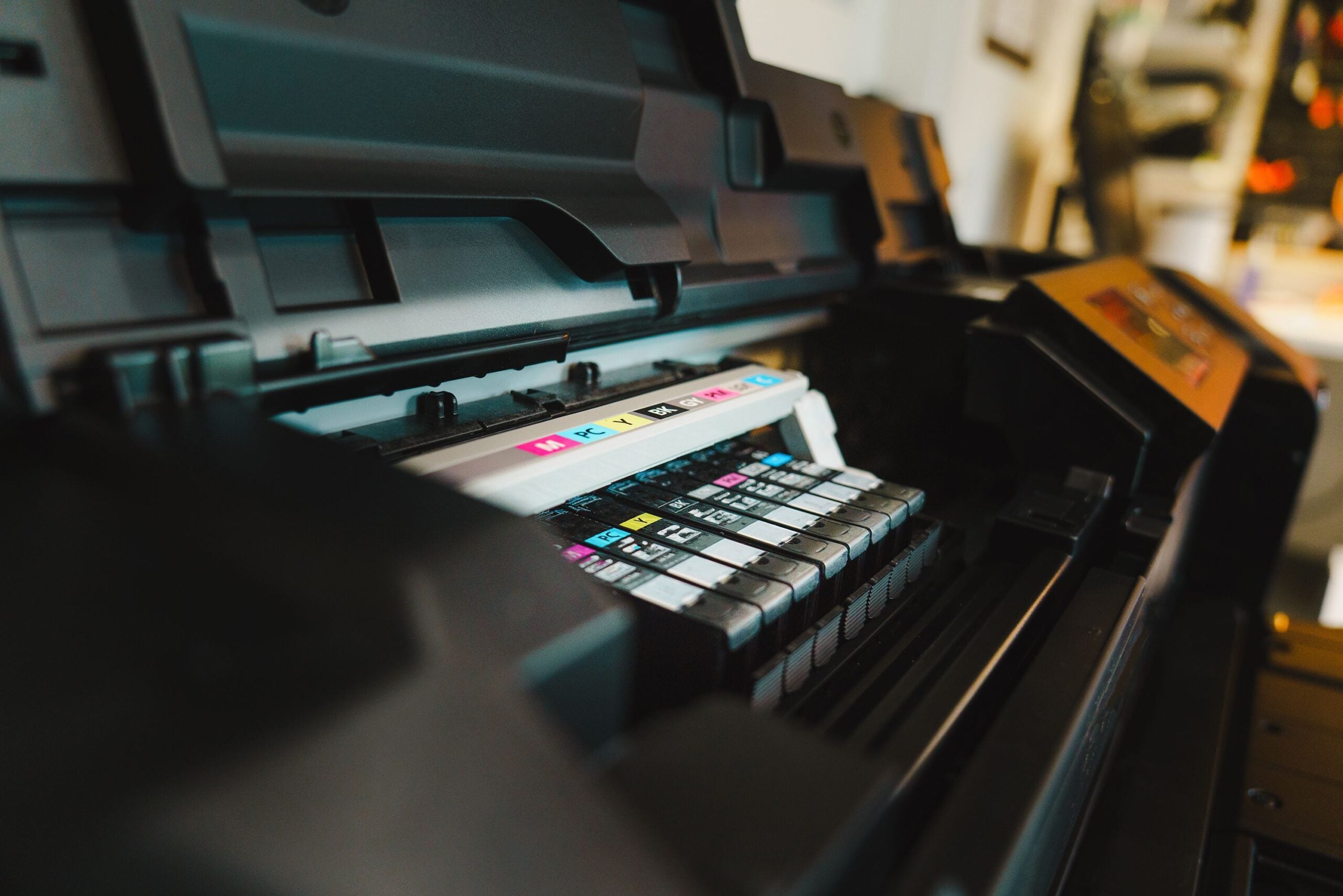 Close-up of an open printer showing several ink cartridges arranged in a row, each labeled with different colors like cyan, magenta, yellow, and black. The surrounding printer parts are slightly out of focus.