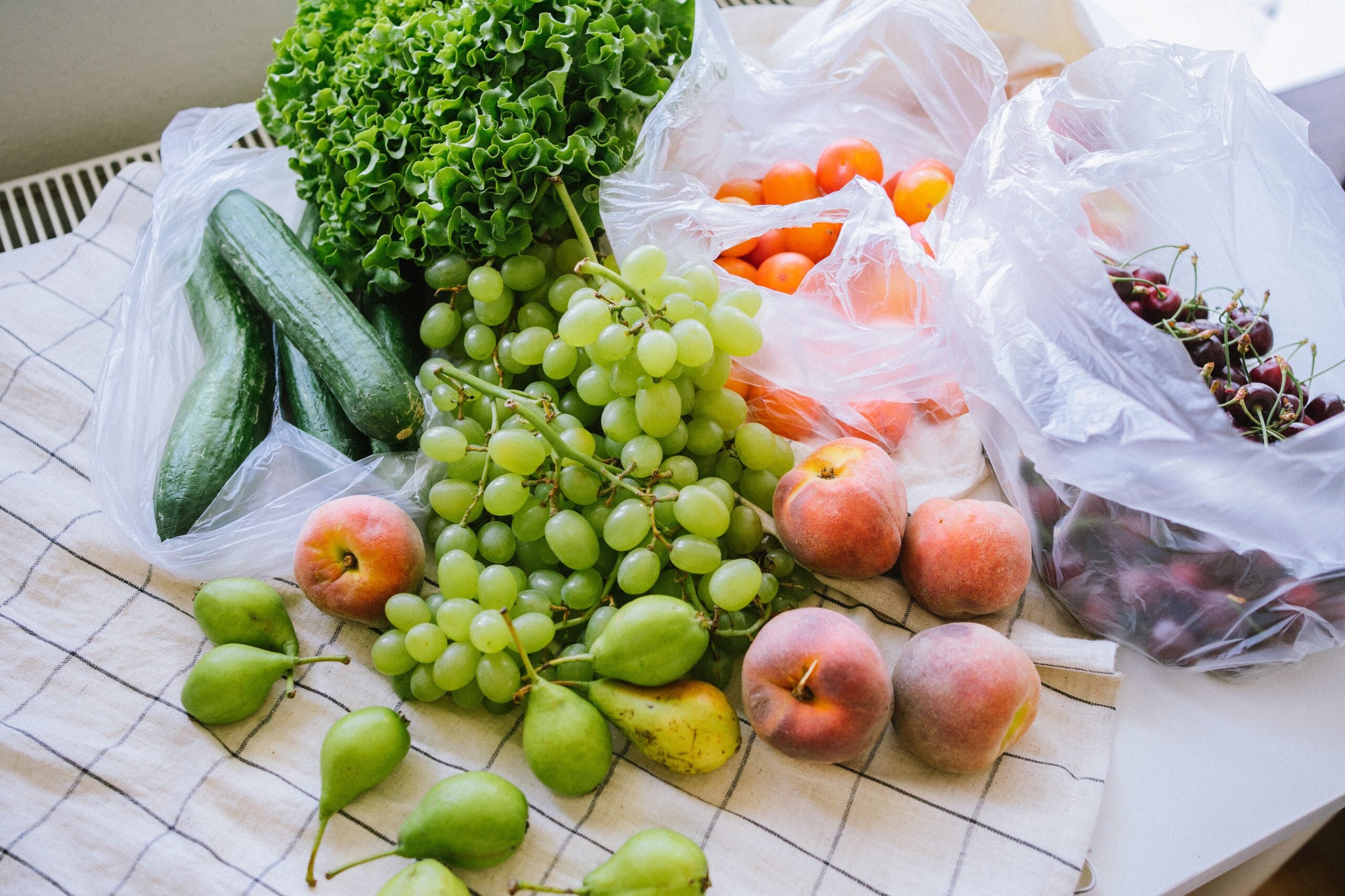 Fresh produce on a cloth, including green grapes, peaches, pears, lettuce, cucumbers, yellow tomatoes, and a plastic bag with cherries.