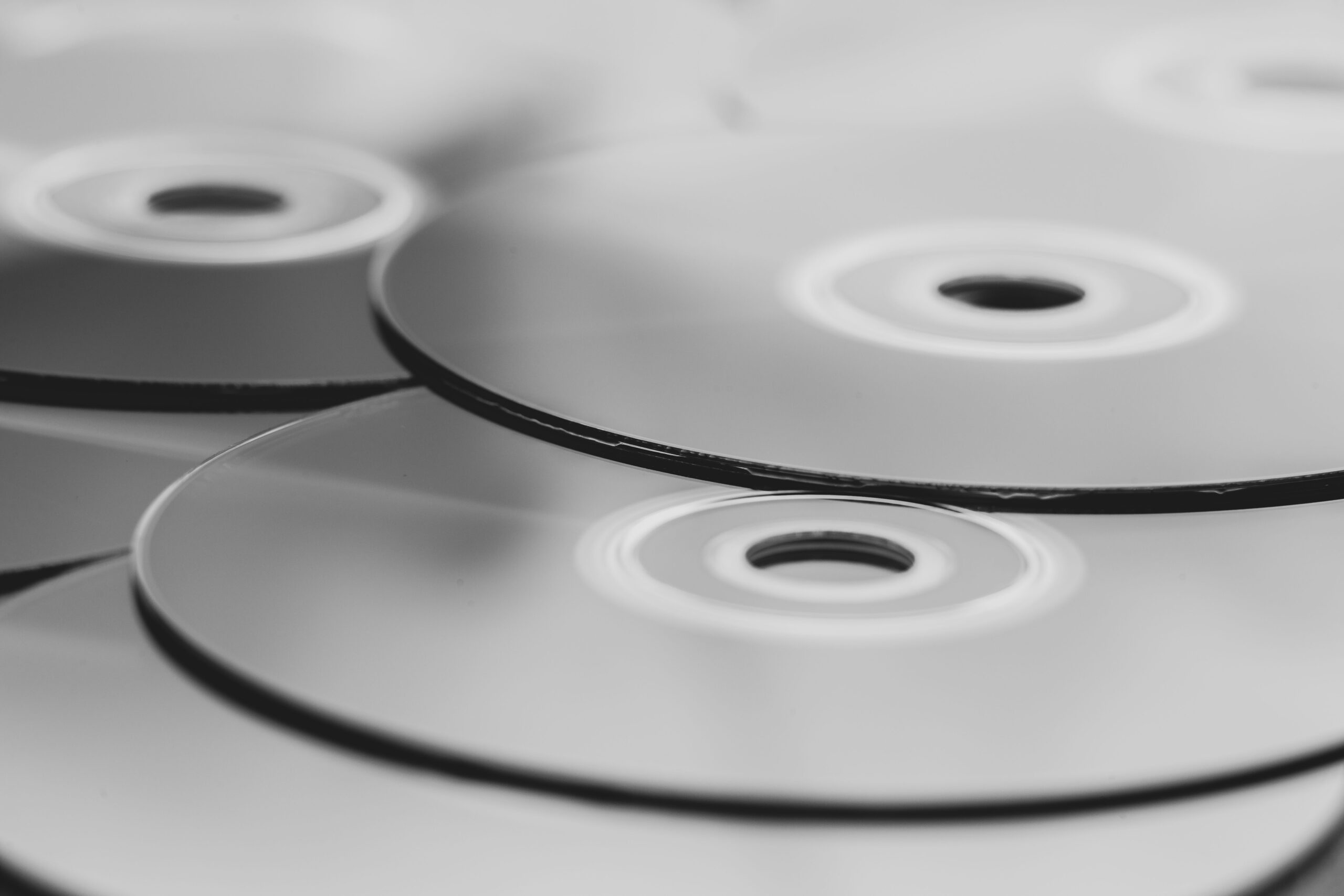 Close-up of several overlapping compact discs (CDs) in black and white, showing circular shapes and reflective surfaces.