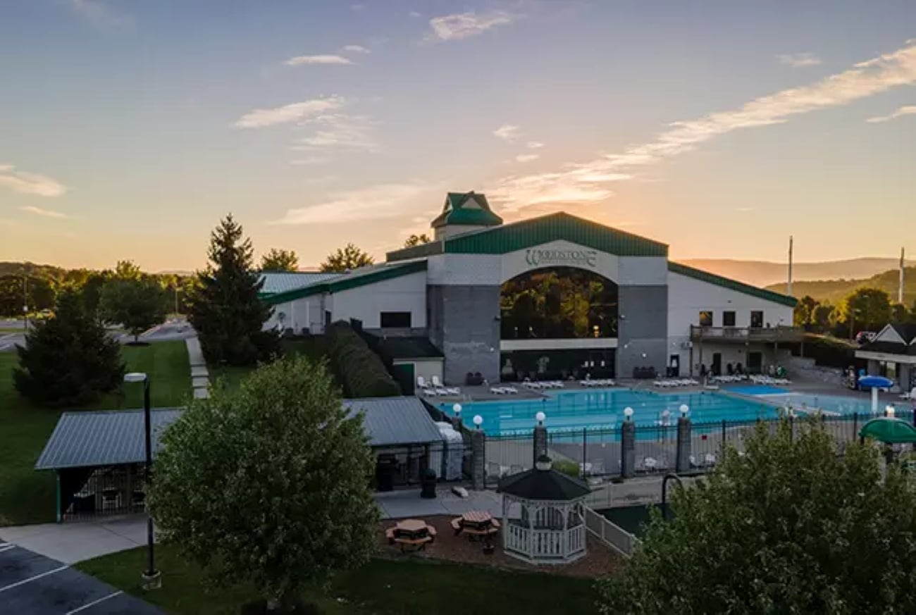 A large outdoor swimming pool at one of the region’s premier resorts, with a nearby gazebo, trees, and a pavilion-style building in the background, photographed at sunrise beneath a partly cloudy sky.