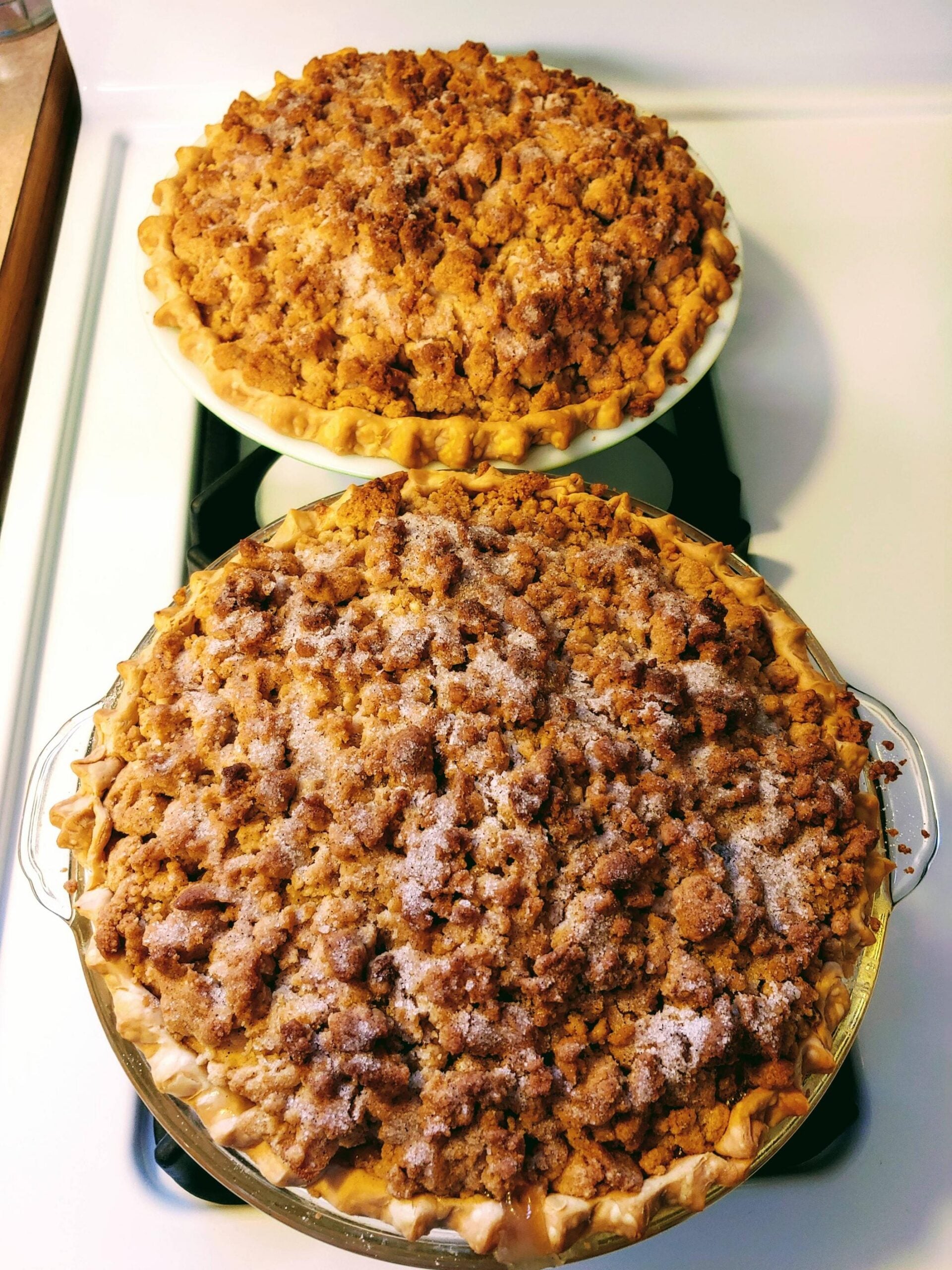 Two freshly baked pies with crumbly brown sugar streusel topping, sitting on a stovetop. The crusts are golden brown, and a light dusting of sugar is visible on top.