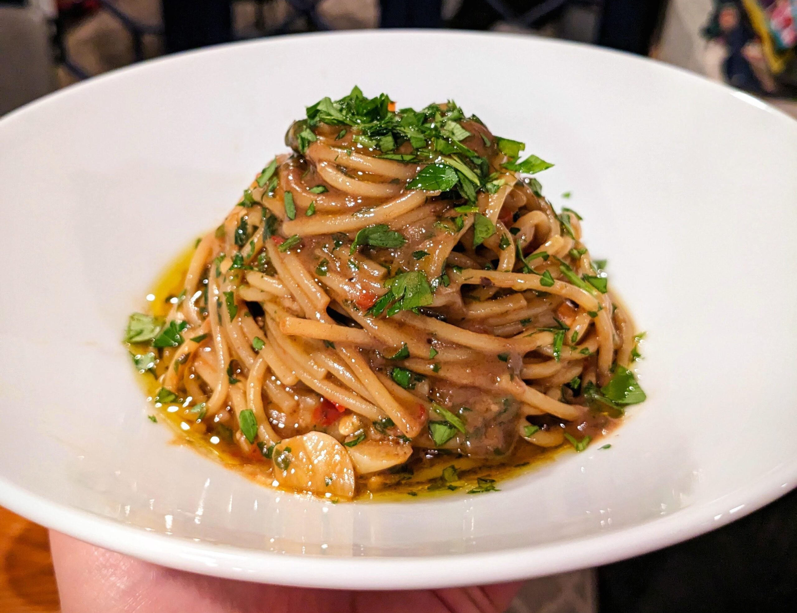 A white bowl filled with spaghetti in a rich sauce, garnished with fresh chopped parsley—perfect for those who appreciate stunning photos of pasta.