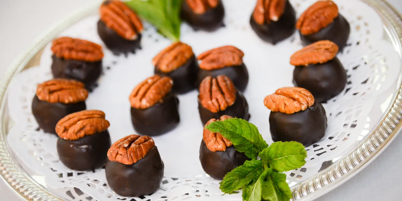 A silver platter holds several chocolate-covered turtle candies, the best souvenir, each topped with a pecan half and garnished with sprigs of fresh mint.