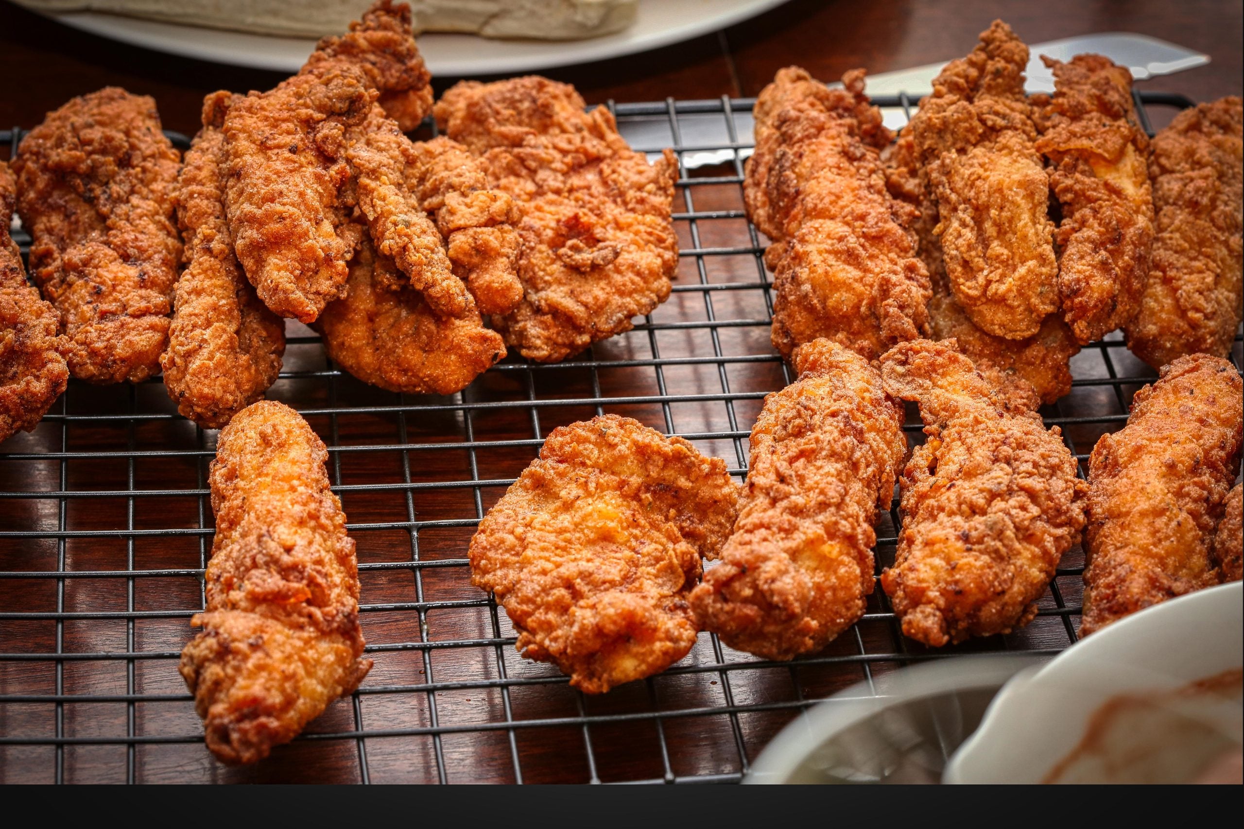 Many pieces of golden-brown crispy fried chicken resting on a wire cooling rack.