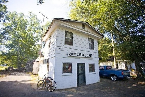 A two-story white building labeled “Jones Bar-B-Q Diner” with a bicycle parked out front and a blue pickup truck parked to the side.