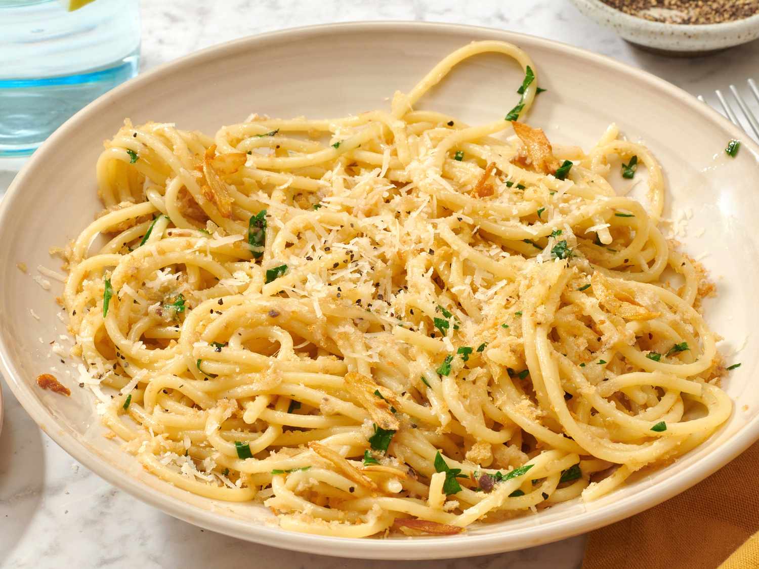 A bowl of spaghetti topped with grated cheese, herbs, and toasted garlic.